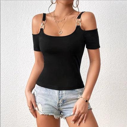 Woman wearing black off-shoulder top with gold buckle straps and denim shorts against white wall
