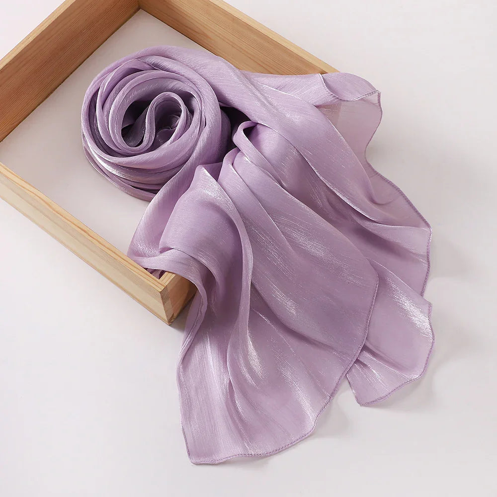 Light purple shiny chiffon scarf rolled and flowing inside a light wooden box on white surface