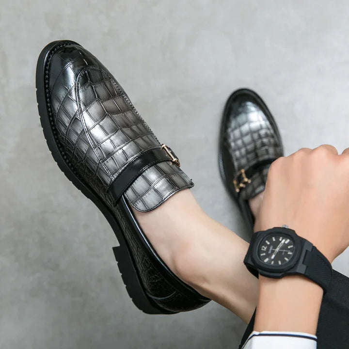 Black and silver men’s loafers with crocodile texture and gold buckle detail on feet