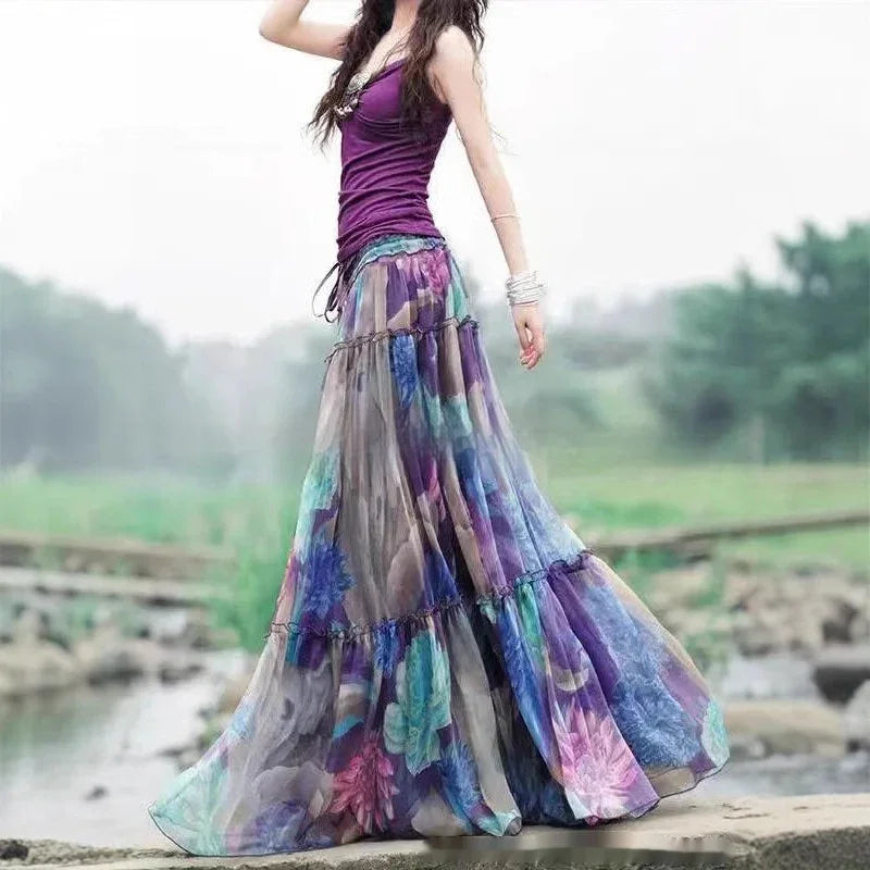 Woman in purple tank top and flowing colorful floral maxi skirt outdoors by water and stone path