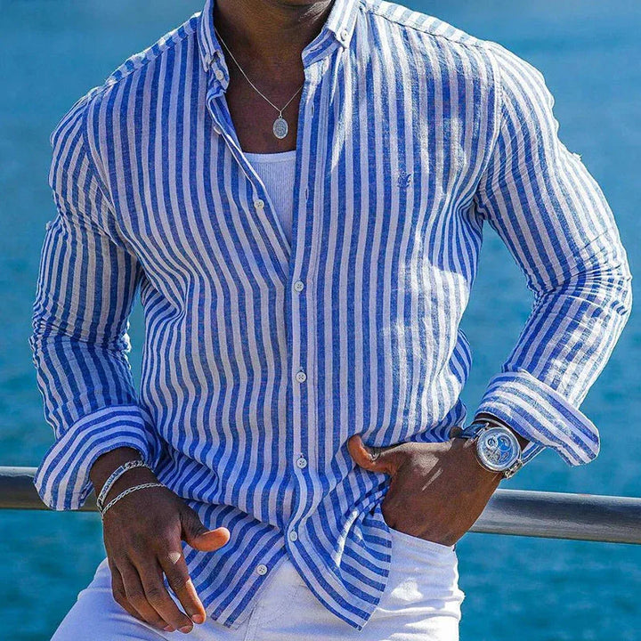 Man wearing blue and white striped button-down shirt with silver watch and necklace by ocean