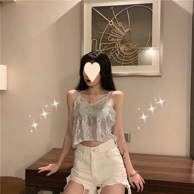 Woman wearing silver sequin tank top and white denim shorts indoors by wooden table with abstract artwork