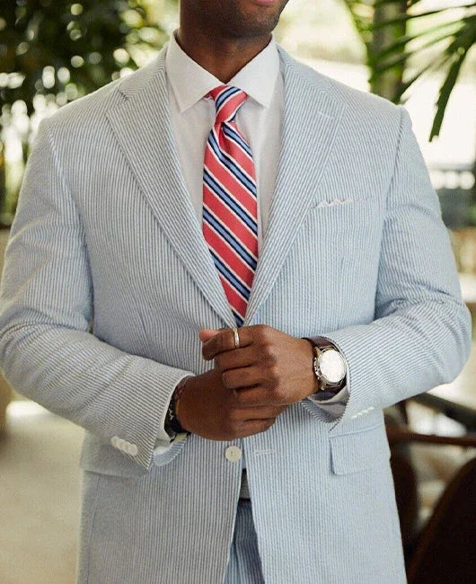 Man wearing light blue seersucker suit with white shirt and red striped tie in indoor setting