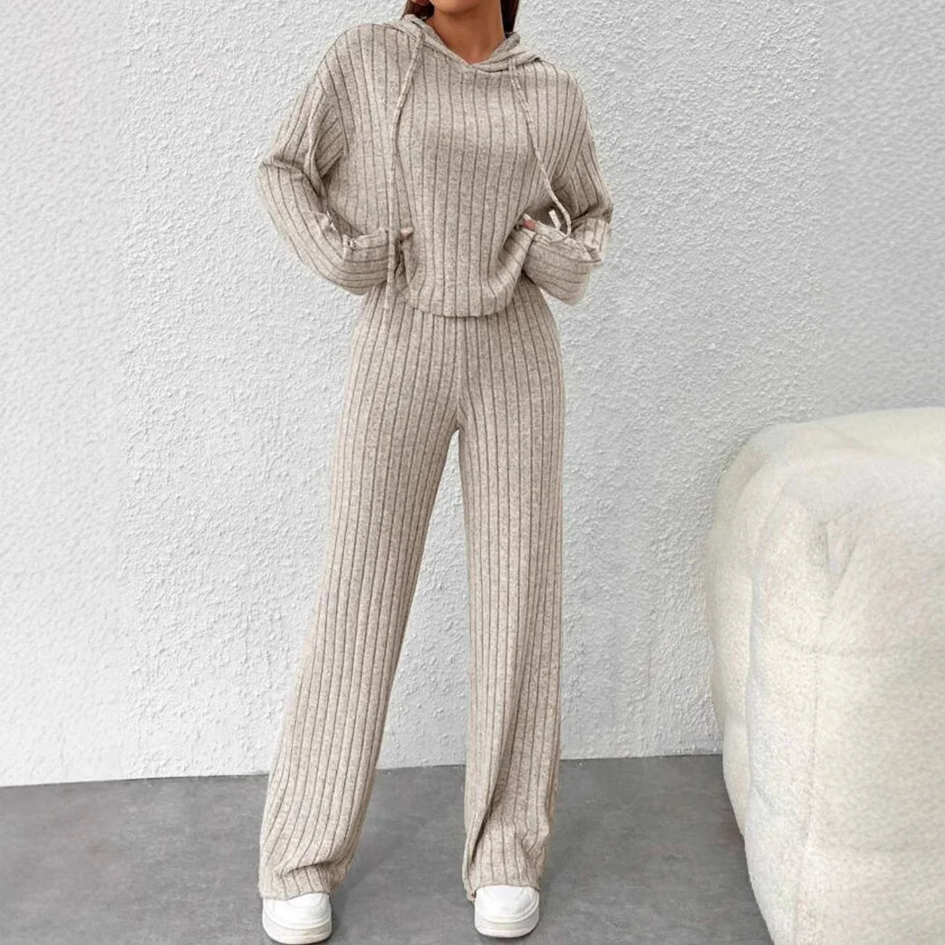 Woman in beige ribbed knit hoodie and wide-leg pants set with white sneakers against white textured wall