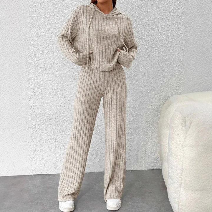 Woman in beige ribbed knit hoodie and wide-leg pants set with white sneakers against white textured wall