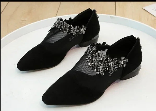 Elegant black flats with mesh and rhinestone floral embellishments on white tray