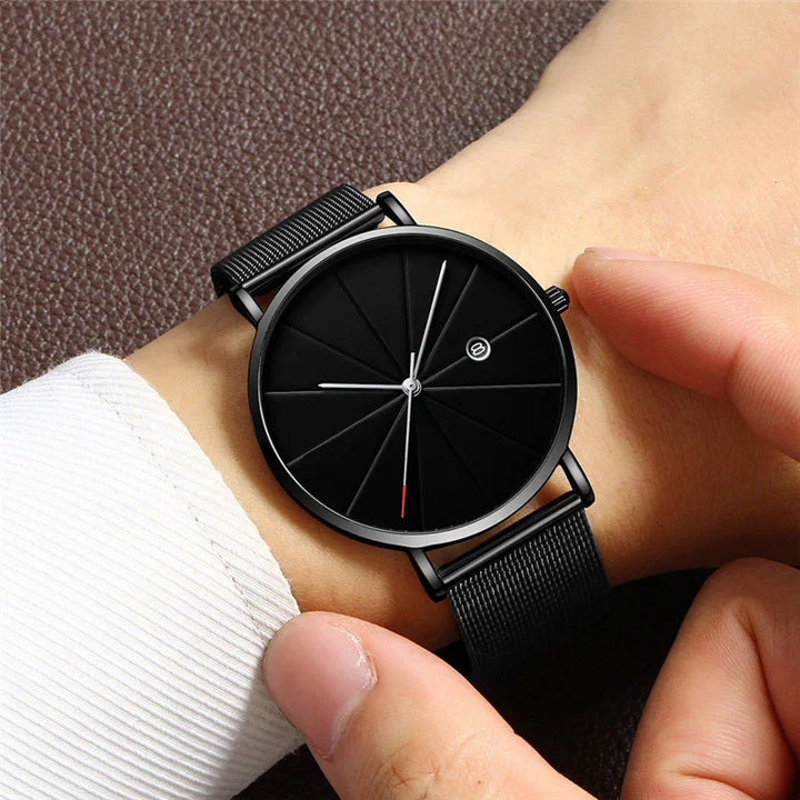 Minimalist black wristwatch with textured dial and black mesh strap worn on wrist