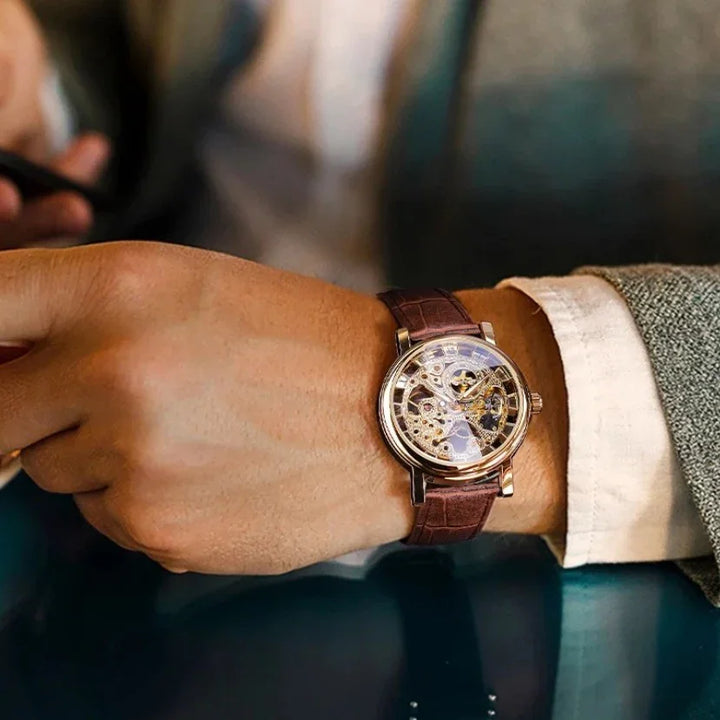 Luxury men's skeleton wristwatch with brown leather strap on a suited wrist