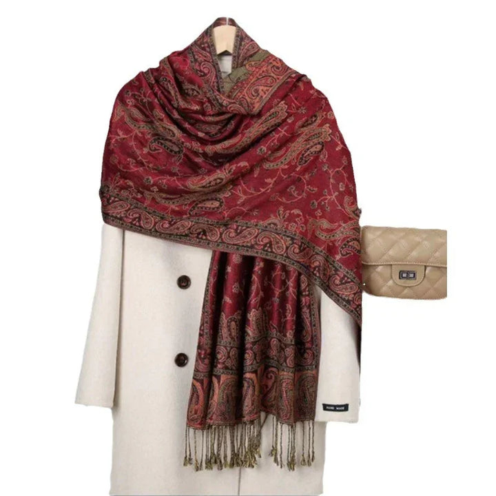 White wool coat with brown buttons draped by red paisley patterned shawl and beige quilted leather handbag