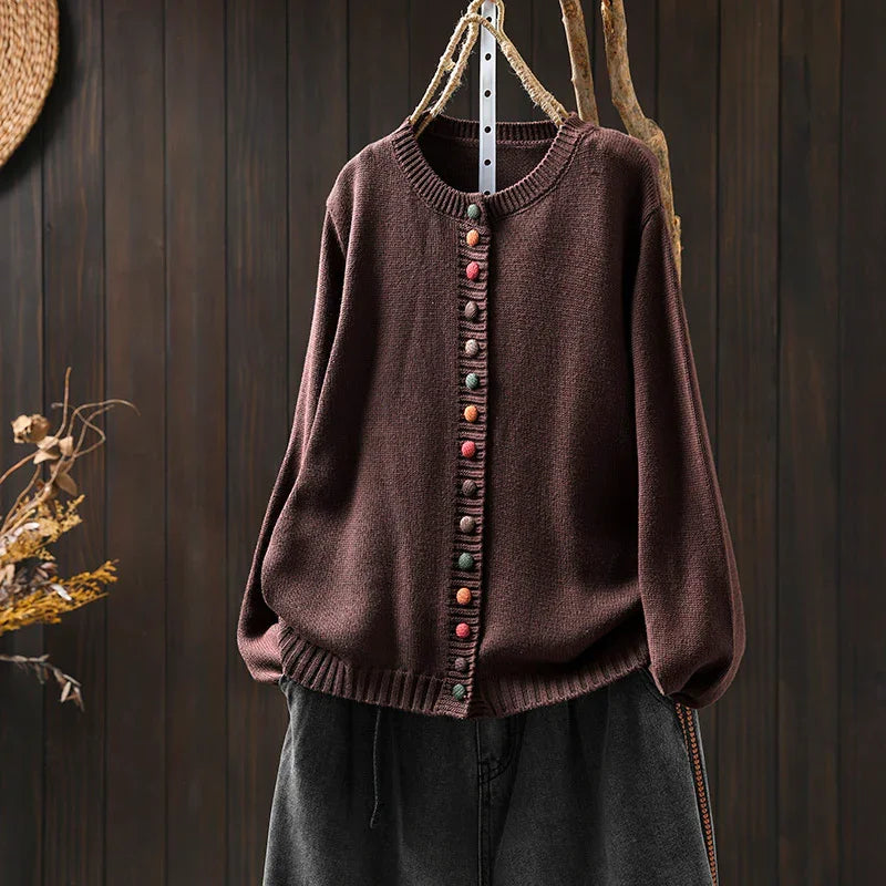 Brown knitted cardigan with colorful round buttons hanging on wooden background