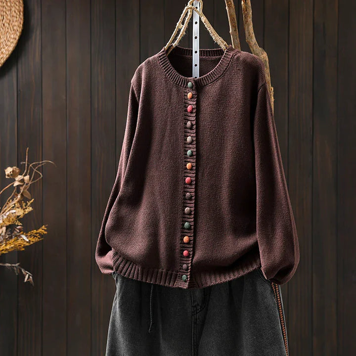 Brown knitted cardigan with colorful round buttons hanging on wooden background