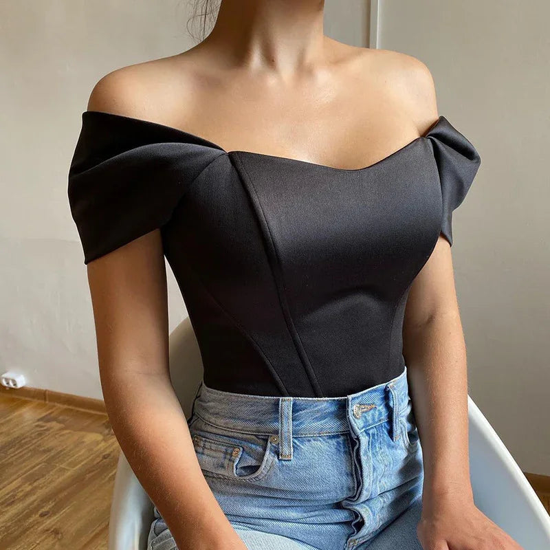 Woman wearing black off-shoulder top with structured sleeves paired with high-waisted blue jeans