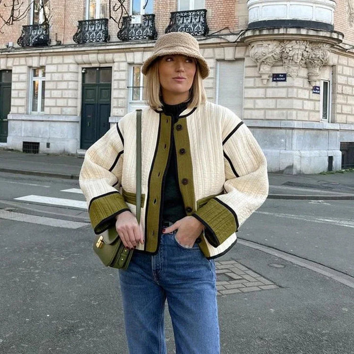 Woman wearing a cream and olive quilted jacket, bucket hat, and blue jeans standing on a city street
