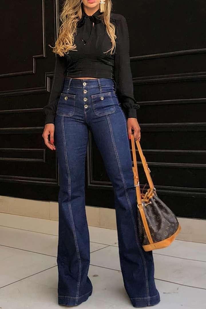 Woman wearing high-waisted dark blue flared jeans and a black long-sleeve crop top holding designer handbag