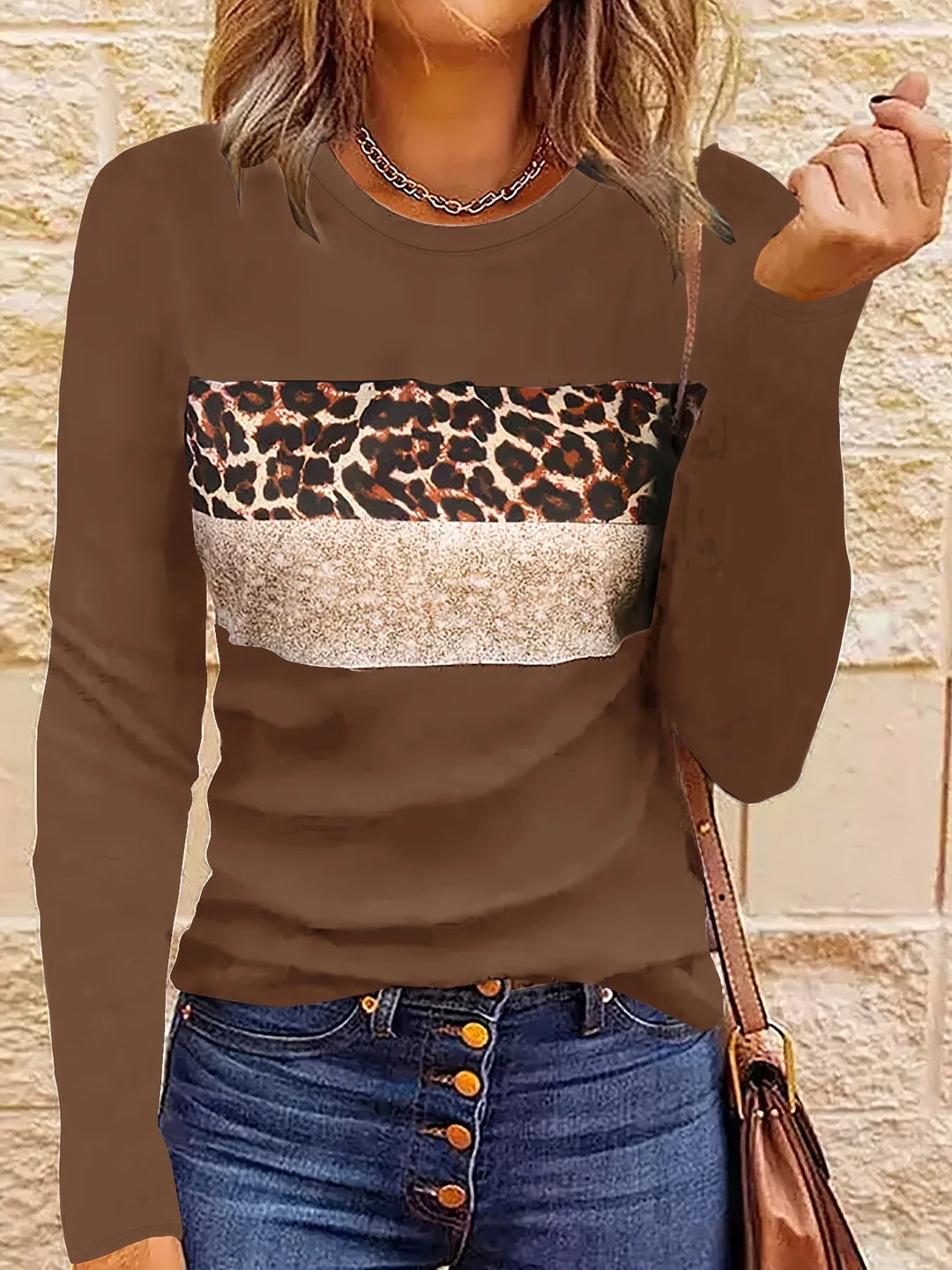 woman wearing brown long-sleeve top with leopard print and beige panel, paired with blue jeans and brown shoulder bag