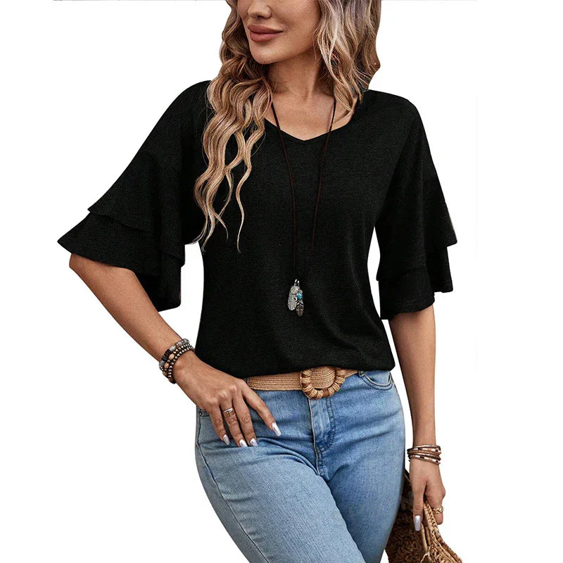Woman wearing black V-neck top with layered ruffle sleeves, blue jeans, hat, and boho jewelry