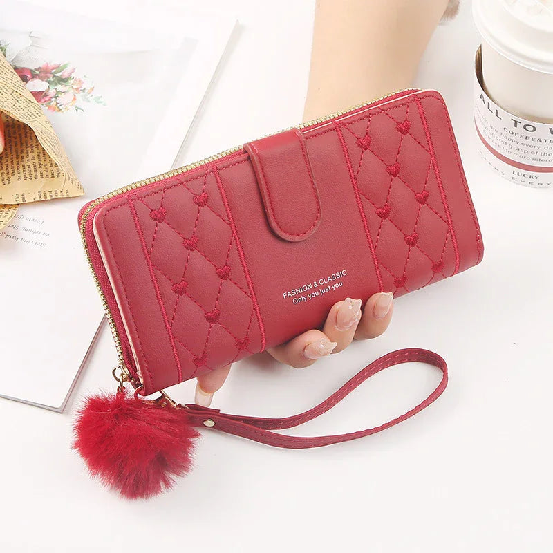Red quilted leather wallet with wrist strap and fluffy pom-pom accessory held in hand on white background