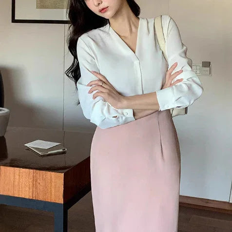 woman wearing white blouse and light pink pencil skirt standing indoors near wooden table