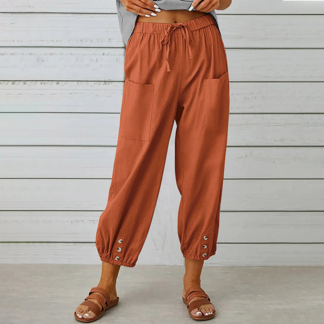 Woman wearing rust orange casual drawstring pants with front pockets and buttoned cuffs, standing indoors