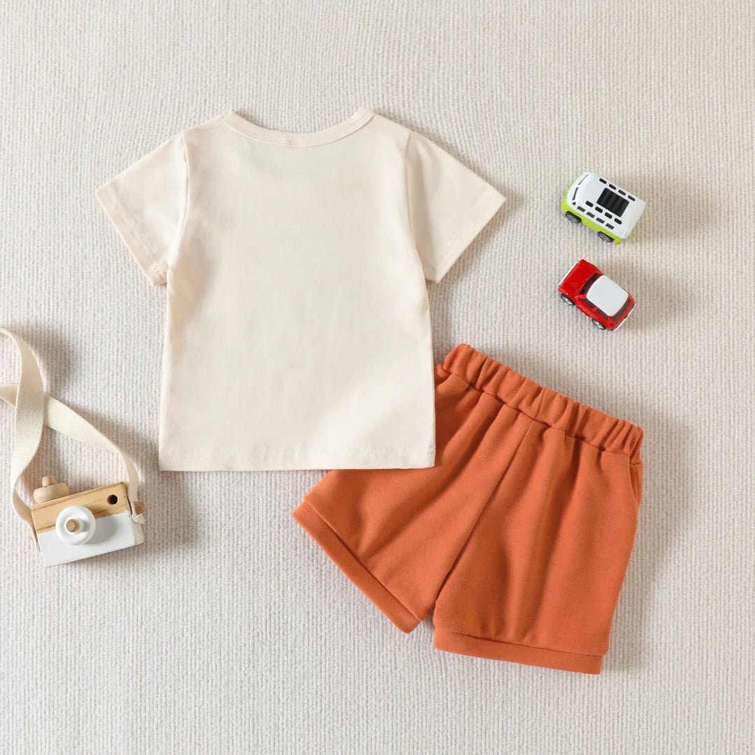Cream short sleeve toddler t-shirt and rust orange shorts with toy wooden camera and small toy cars