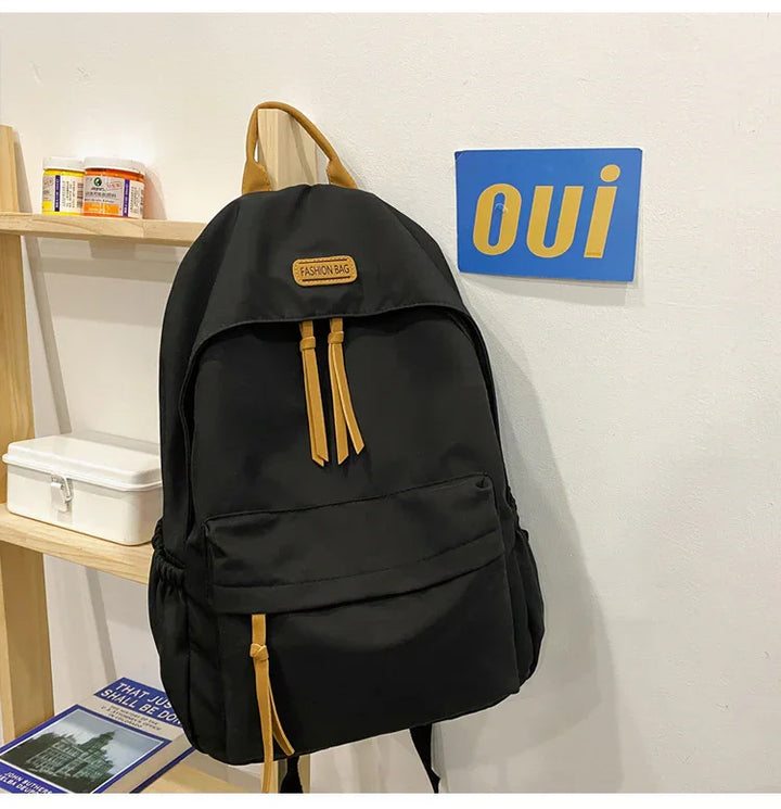 Black fashion backpack with brown leather accents hanging on a wall near wooden shelf and blue 'oui' sign