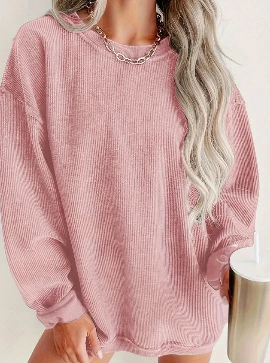 Woman wearing oversized pink ribbed sweater with long wavy blonde hair and silver chain necklace