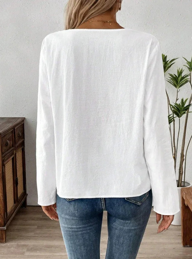 Woman wearing plain white long-sleeve top and blue jeans standing indoors with wooden furniture and plants