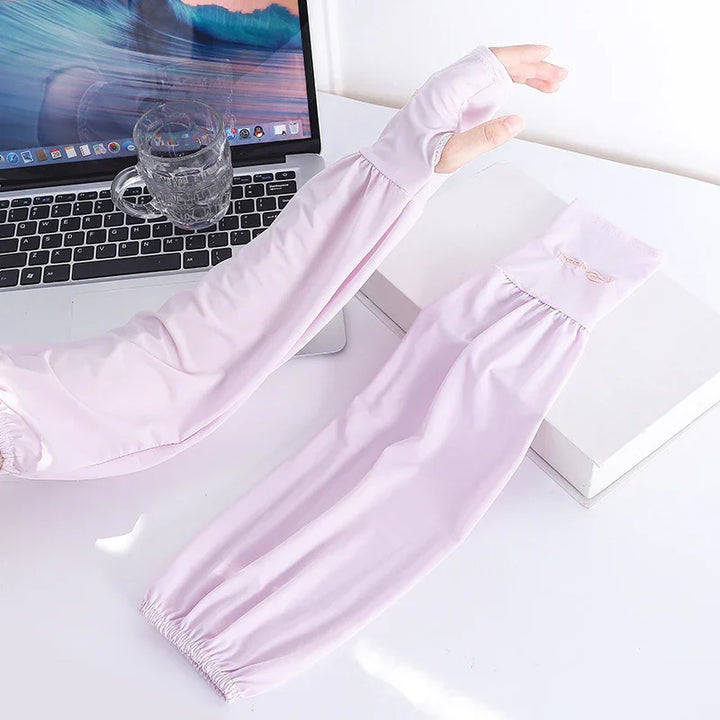 Light pink sun protection arm sleeves, one worn on hand with thumb hole, placed beside laptop and glass