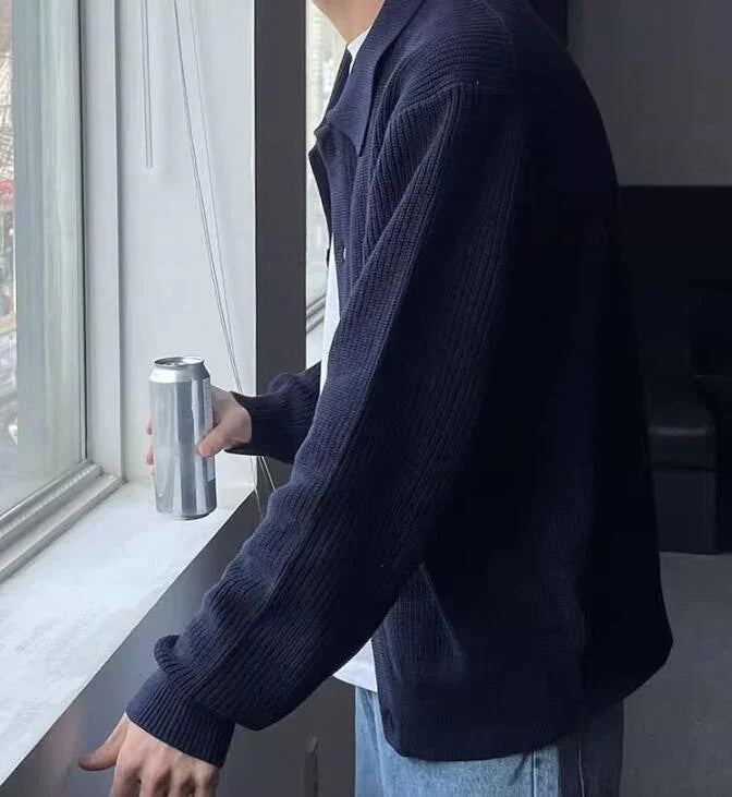 Person wearing a dark navy knit sweater holding a silver can by a window in a modern room