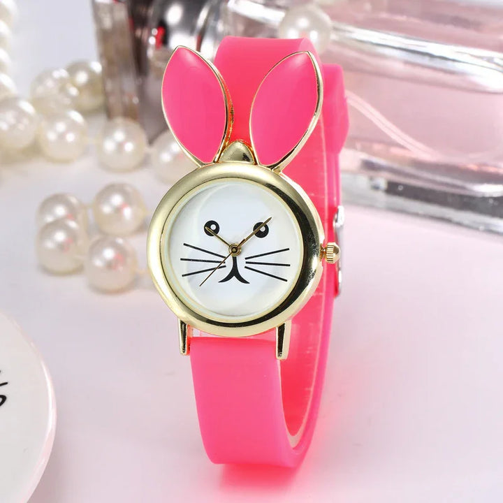 Pink silicone wristwatch with gold bunny ears and a cute rabbit face dial, pearls in background