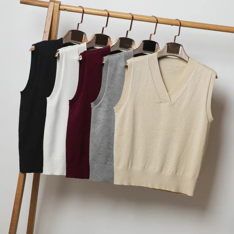 Knitted sleeveless vests in black, white, burgundy, gray, and beige hanging on wooden rack
