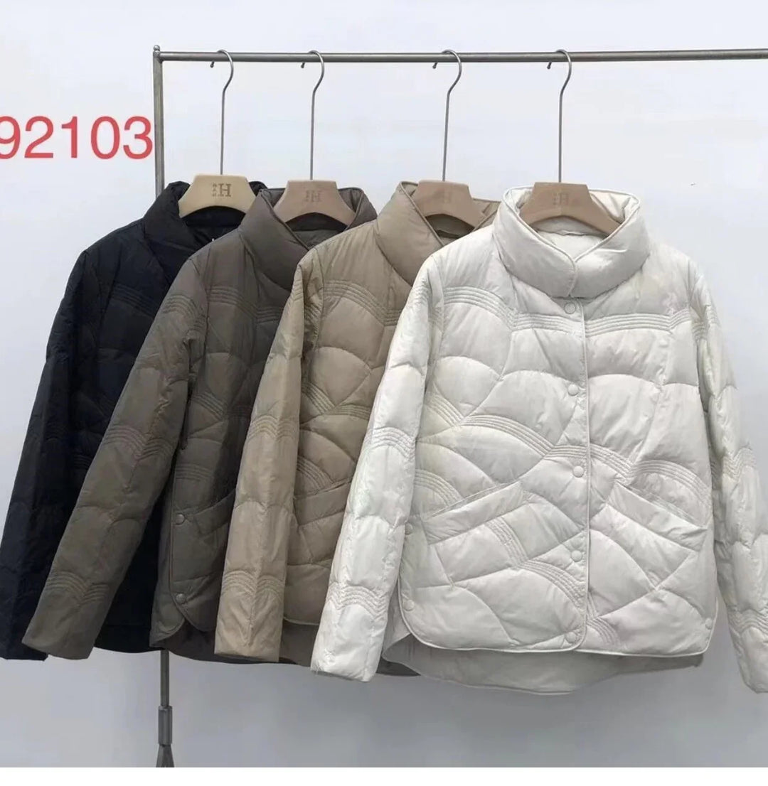 Four quilted winter jackets in black, dark gray, beige, and white hanging on rack with high collars