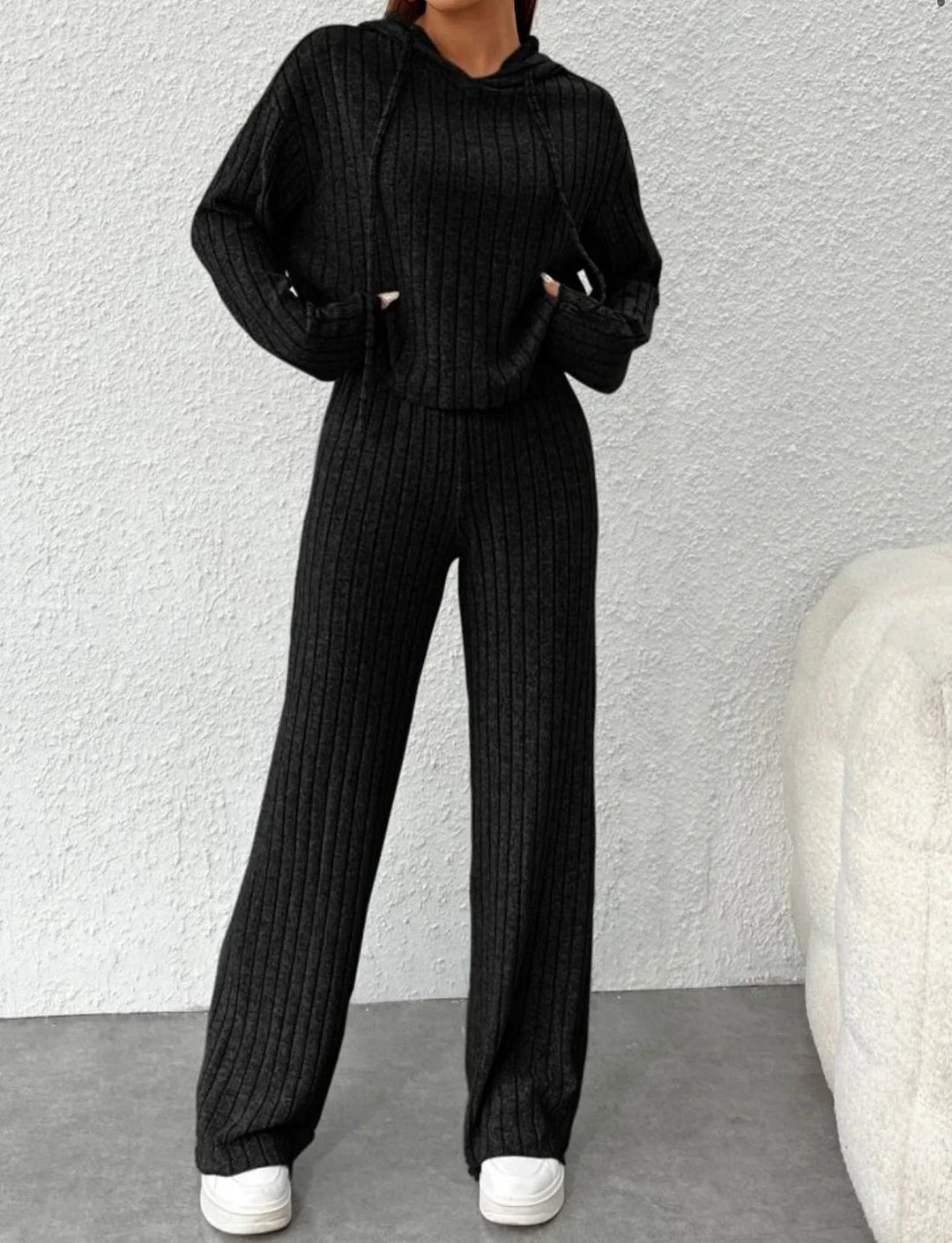 Woman wearing black ribbed knit hoodie and wide-leg pants set with white sneakers indoors