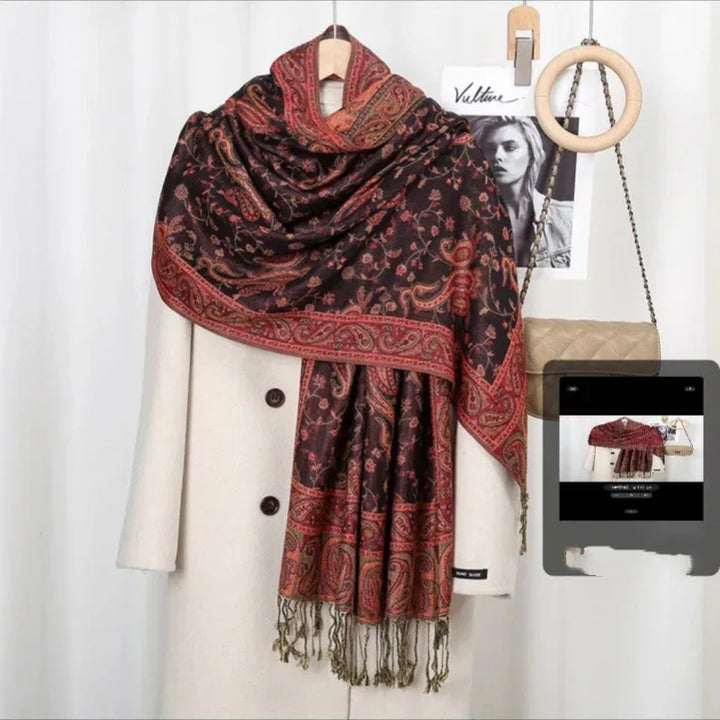 Elegant dark paisley shawl with red and green patterns draped over a cream coat on a hanger