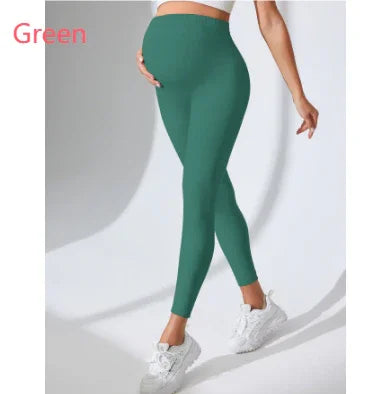 Pregnant woman wearing green maternity leggings and white sneakers on plain background