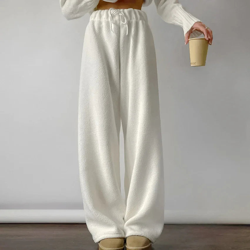 Person wearing white fleece wide-leg sweatpants holding a paper coffee cup in a minimalistic setting