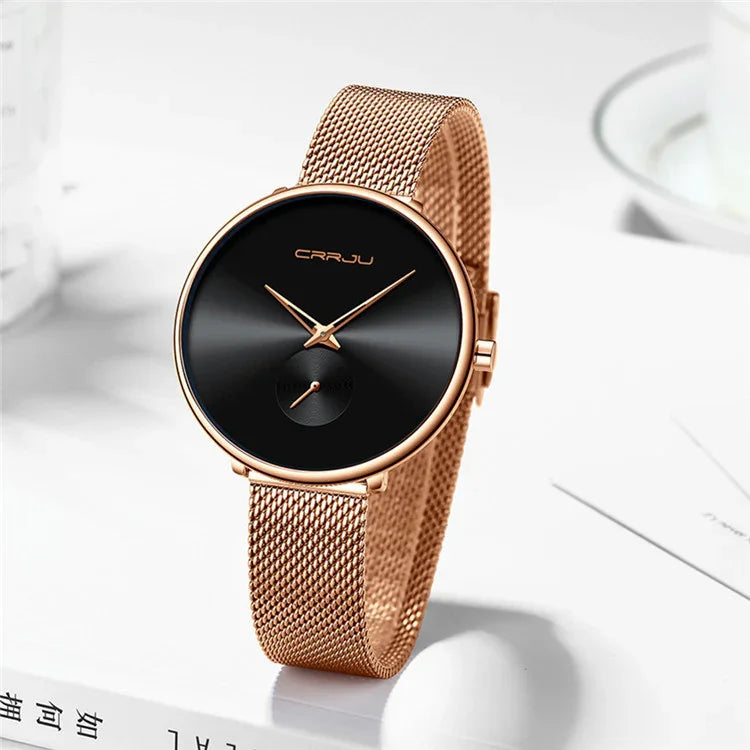 Rose gold mesh band wristwatch with black minimalist dial and gold hands on white surface