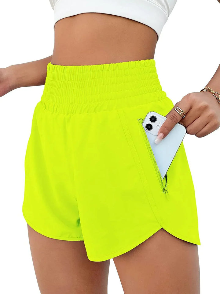 Bright yellow high-waisted athletic shorts with zipper pocket holding a smartphone