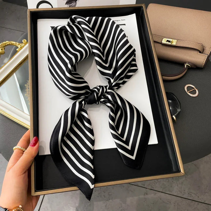 Black and white striped silk scarf tied in a bow inside a gift box on a dark surface