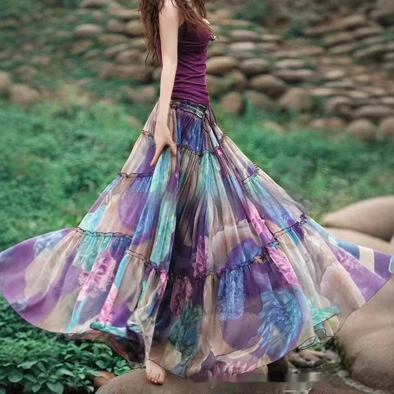 Woman wearing a flowing colorful floral maxi skirt and purple tank top outdoors on greenery and stones