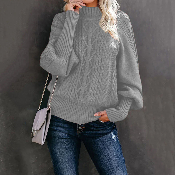 Woman wearing gray cable knit sweater with puff sleeves and dark blue jeans holding a purse