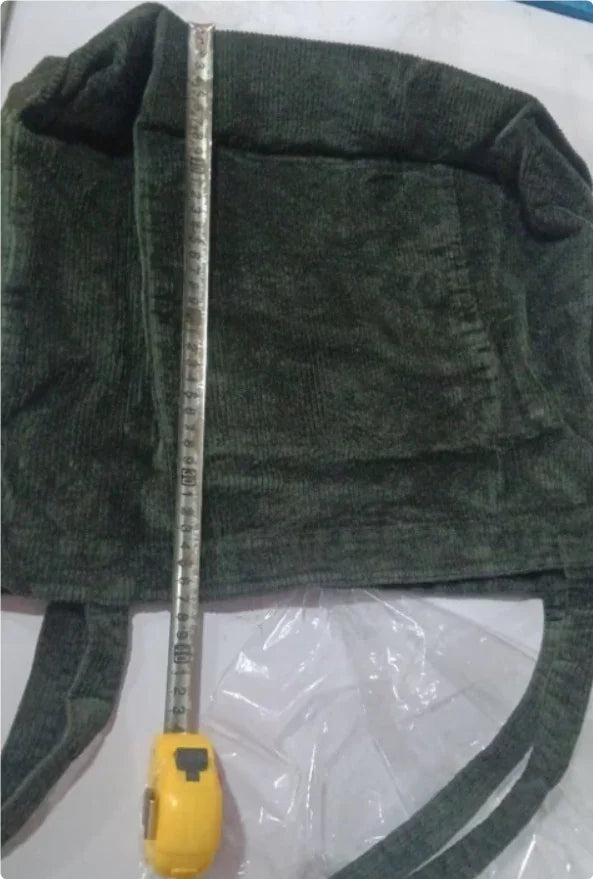 Green corduroy bucket hat with measuring tape showing length on white surface