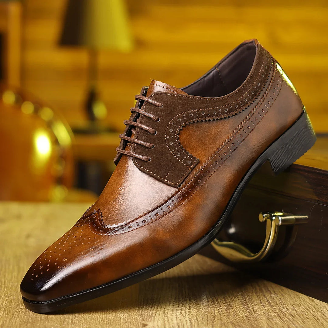 brown men's leather dress shoe with brogue detailing on wooden surface and blurred background
