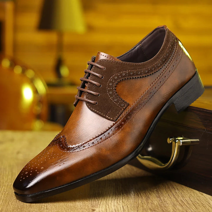 brown men's leather dress shoe with brogue detailing on wooden surface and blurred background