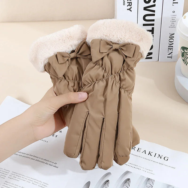 Beige winter gloves with fluffy cuff and decorative bow, held over magazine and books on table