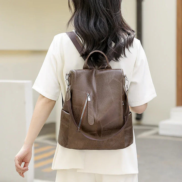 Woman wearing a brown leather backpack with zipper pocket, dressed in white short-sleeve top and pants