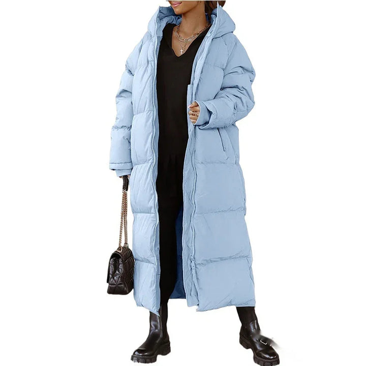 Woman wearing long light blue puffer coat with hood, black dress and boots, holding black handbag