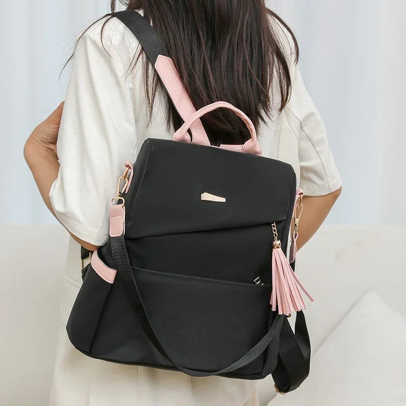 woman wearing black and pink backpack with tassel detail over white outfit indoors