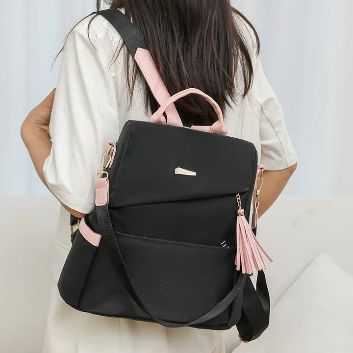woman wearing black and pink backpack with tassel detail over white outfit indoors