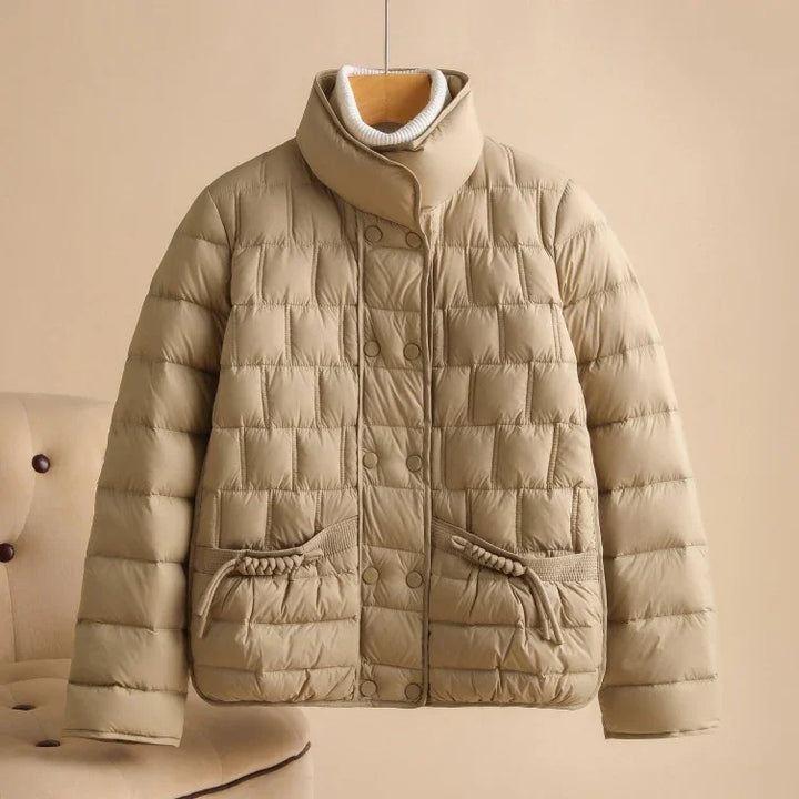 Beige quilted puffer jacket with high collar and front pockets on hanger against neutral background